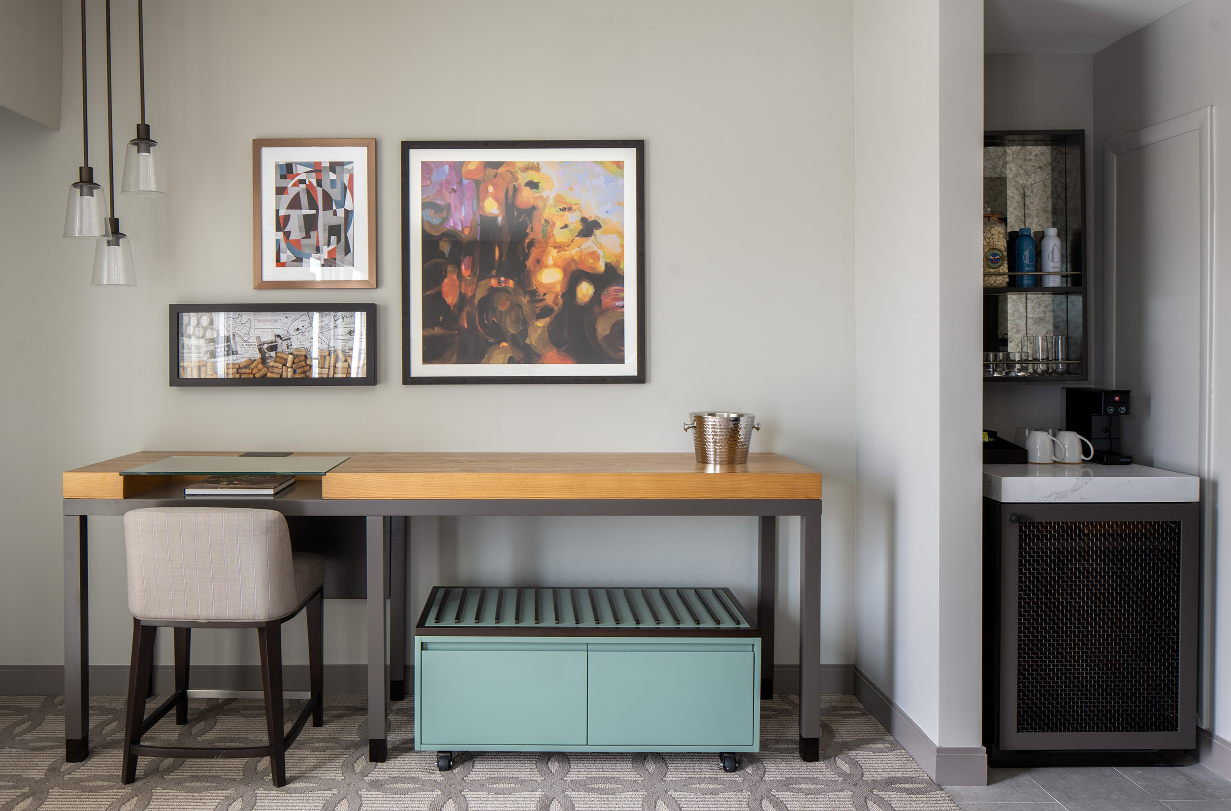 desk with chair on the left, artwork on wall and pantry and beverage station on right